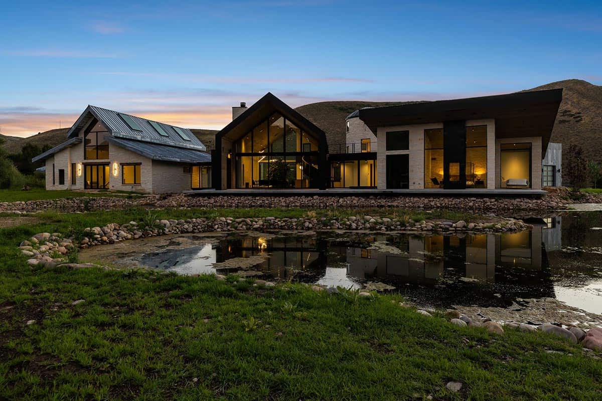 Modern ranch compound at dusk reflected in a stone-edged pond with mountain backdrop