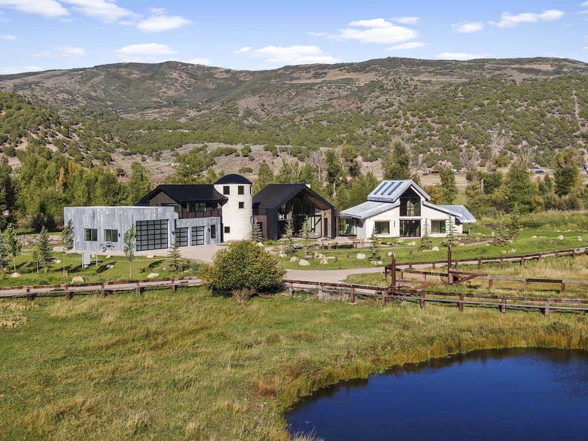 Multi-structure ranch compound with stone tower, metal roof, and pond in a mountain valley