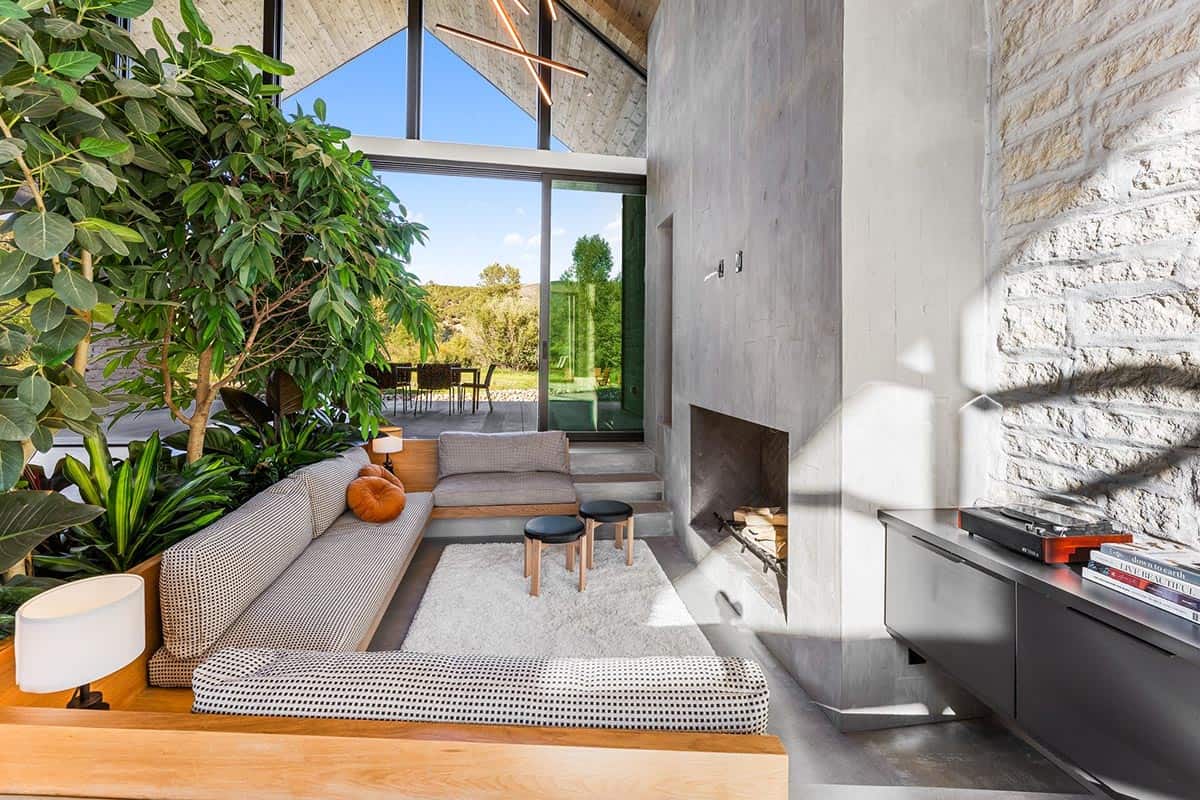 Sunken living room with concrete fireplace, indoor trees, and floor-to-ceiling gable windows