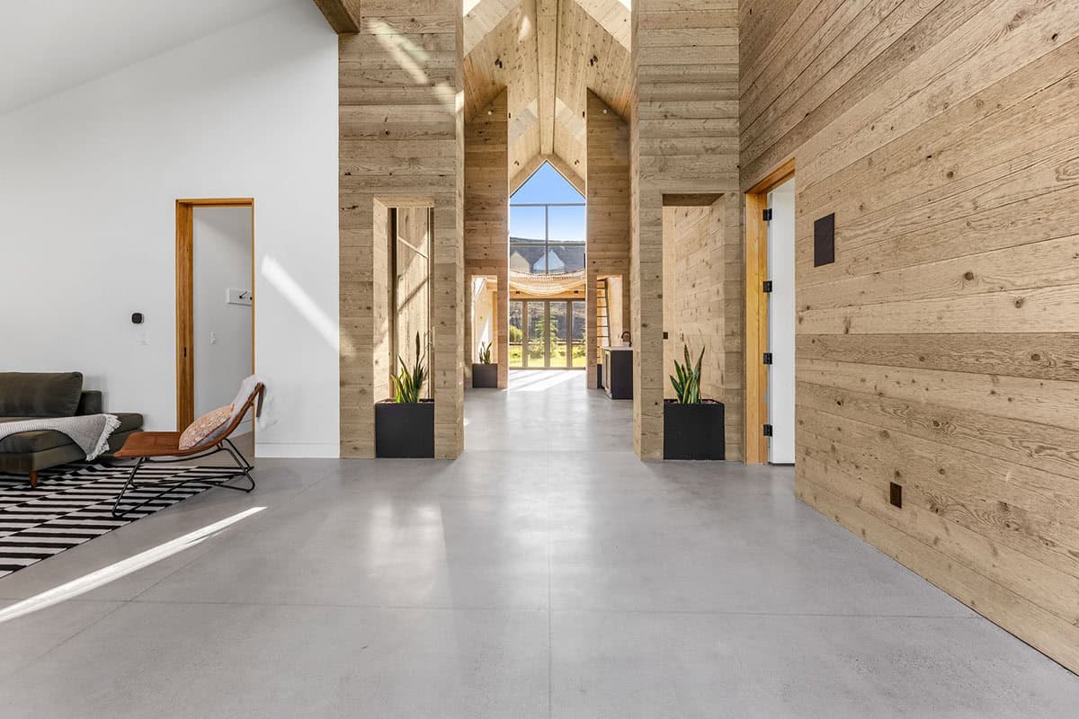 Cathedral-ceiling hallway with wood-clad columns, polished concrete floors, and mountain views