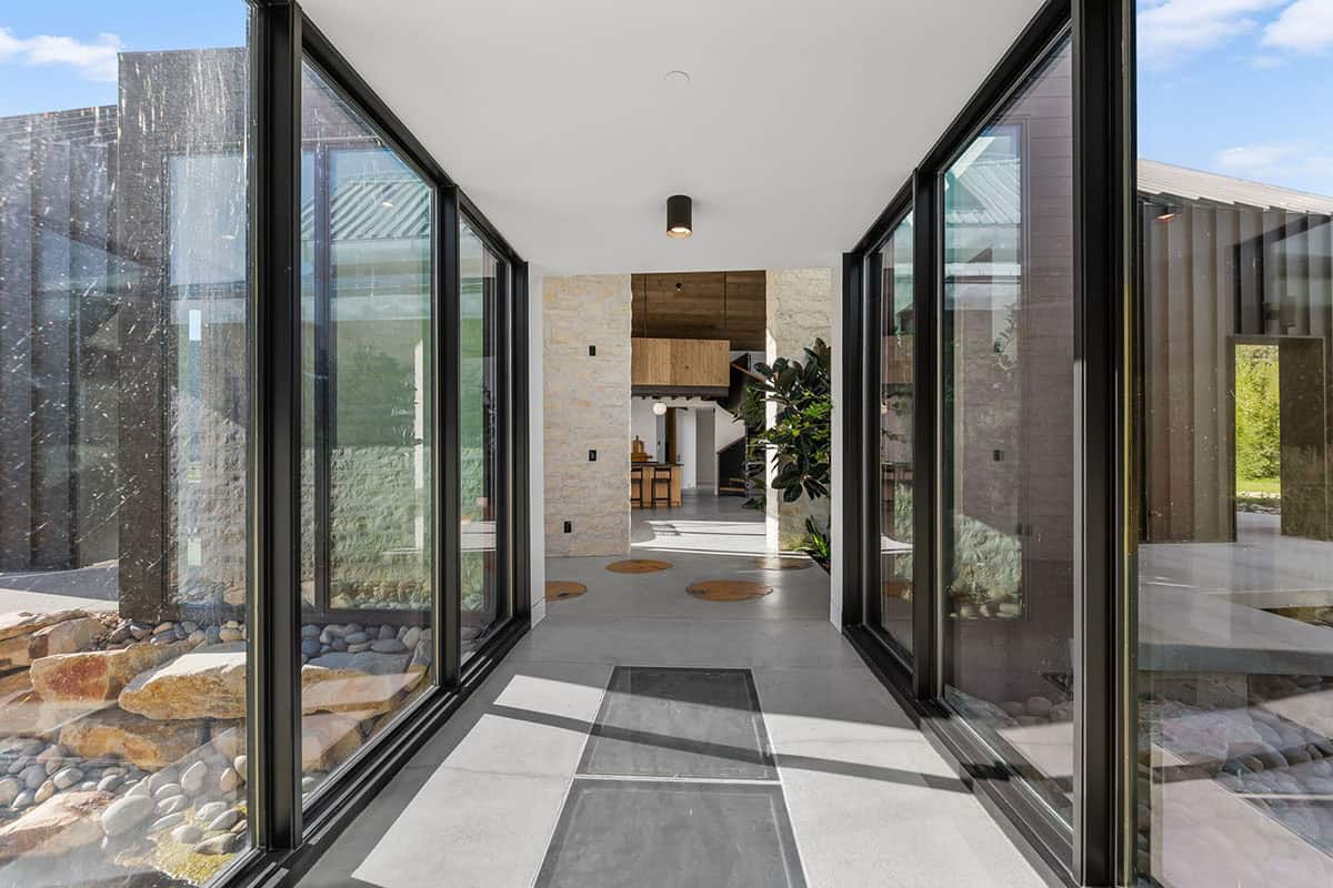 Glass-walled entry corridor connecting dark steel exterior to stone and wood interior