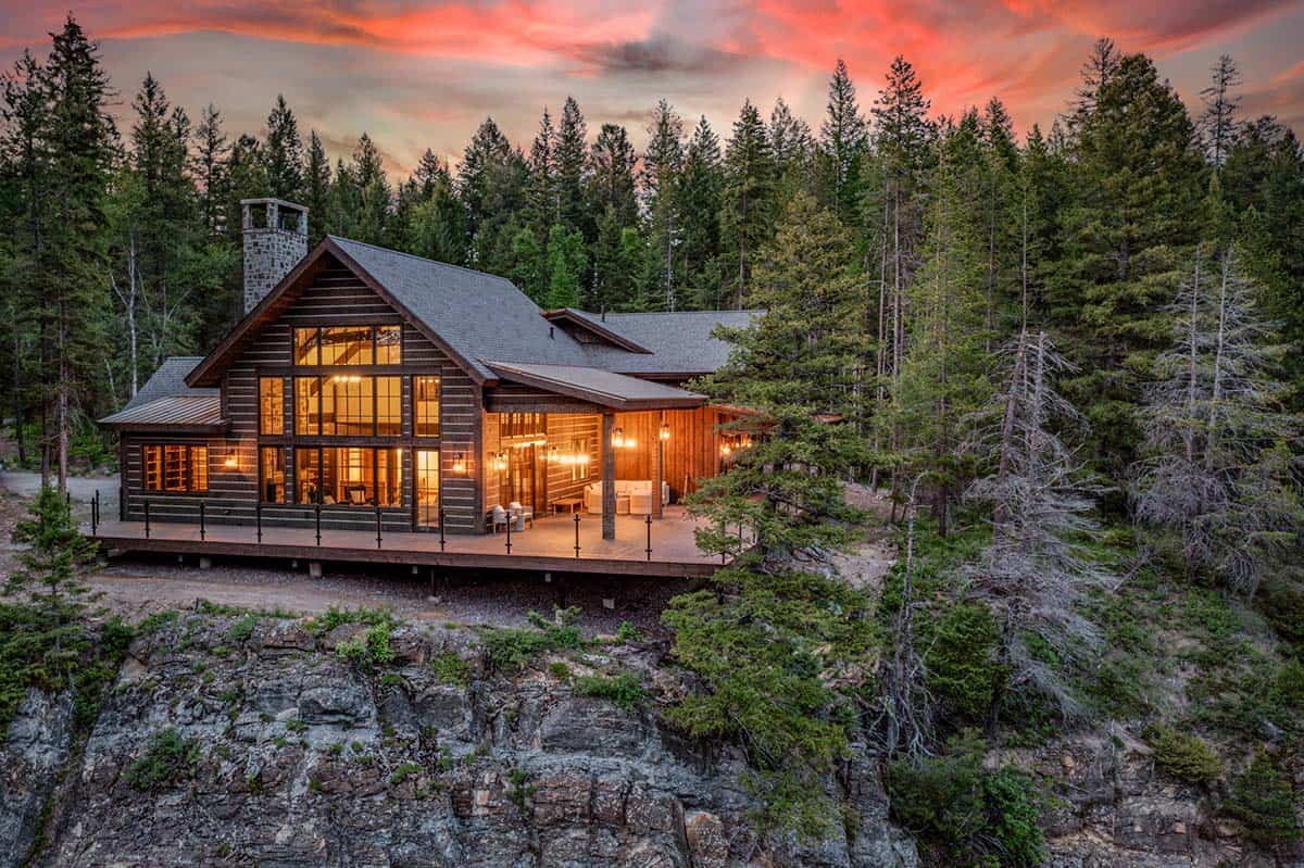 River Dance log cabin at sunset, perched on a rocky cliff above the Flathead River, surrounded by pine forest with warm interior lights glowing