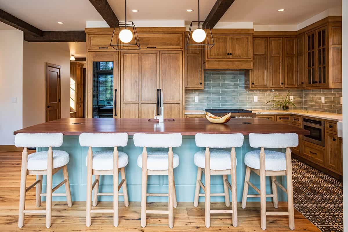 Custom kitchen with warm wood cabinetry, walnut slab island, sage blue base, boucle bar stools, and a sage green tile backsplash