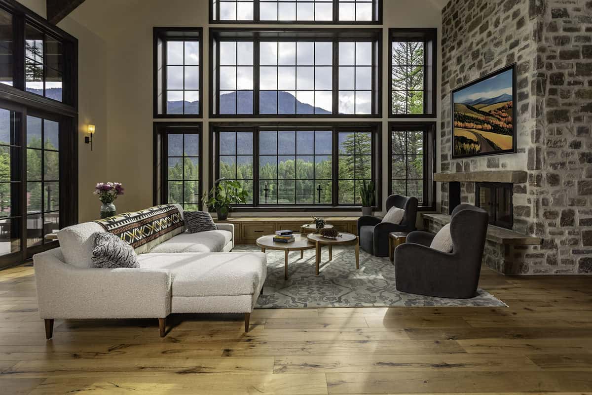 Great room with two-story gridded windows, stone fireplace, white sectional, and sweeping mountain views