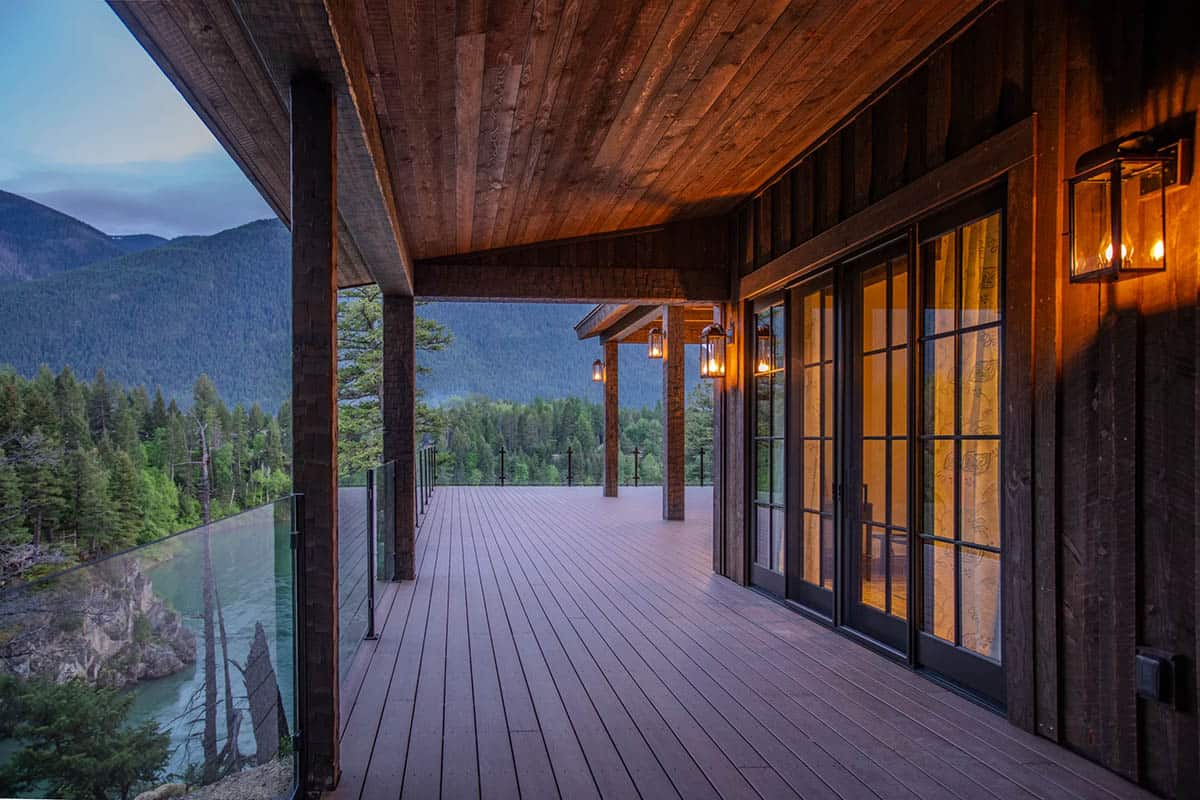 Expansive covered deck at dusk with glass railings, vintage lantern sconces, and panoramic views of the river and mountains below