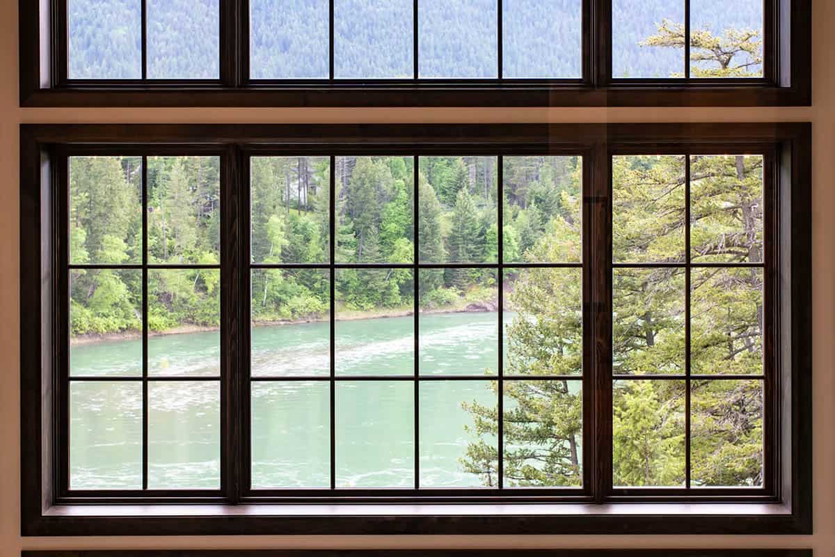 Close-up view through gridded black-framed windows overlooking the rushing turquoise Flathead River and forested riverbank