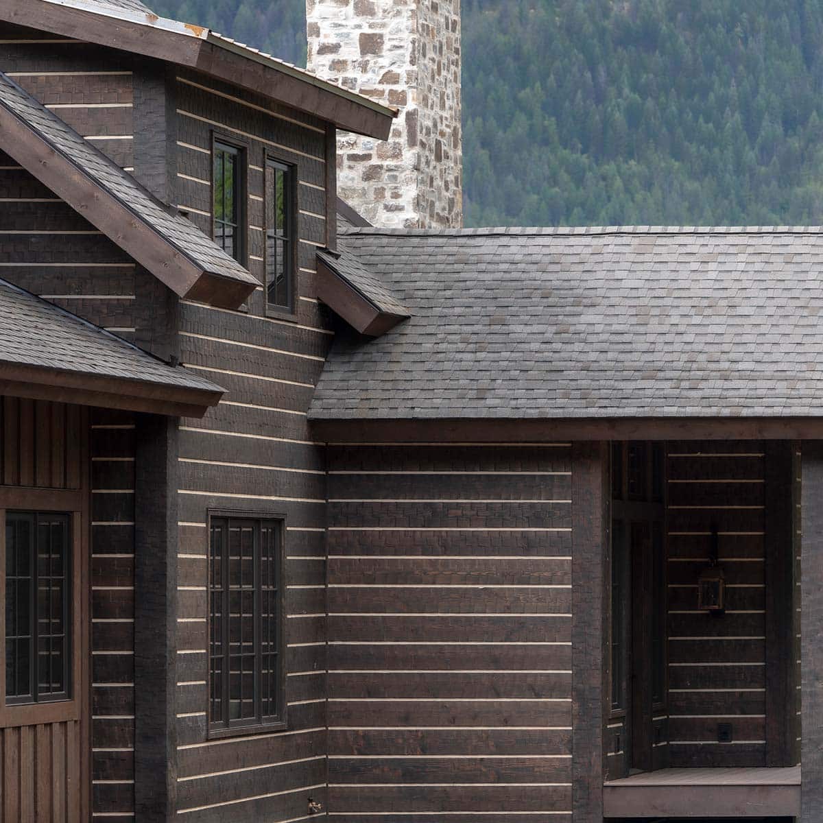 Close-up of hand-hewn log exterior with chinking, stone chimney, and black-framed windows