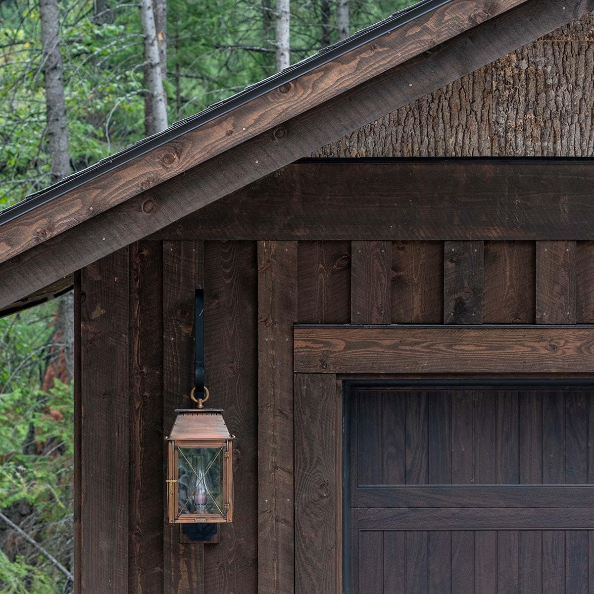 Copper lantern hanging beside the dark wood garage door surrounded by rustic board-and-batten siding