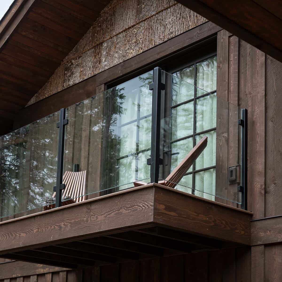 Upper balcony with glass railing, wood deck, and a pair of slatted lounge chairs overlooking the forest