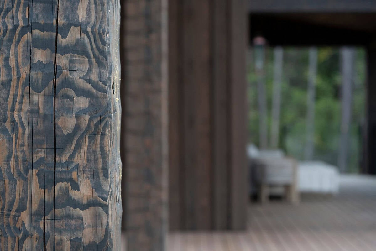 Close-up of a hand-hewn fir timber post with dramatic wood grain, deck and outdoor seating blurred in the background