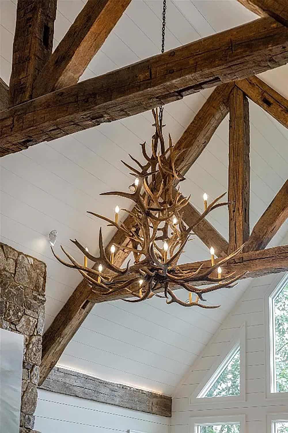 antler chandelier detail, reclaimed wood beam trusses, shiplap vaulted ceiling, stone fireplace