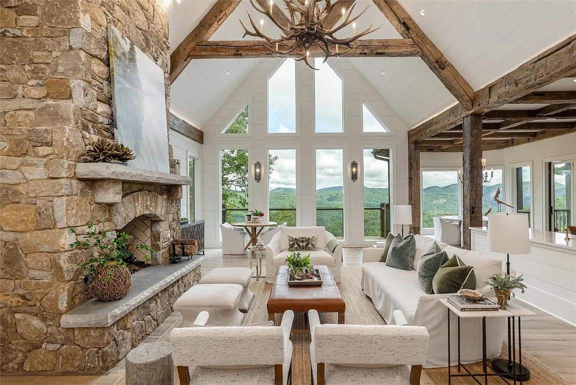 Living room with floor-to-ceiling stone fireplace, antler chandelier, vaulted ceiling with reclaimed wood beams, and panoramic mountain views