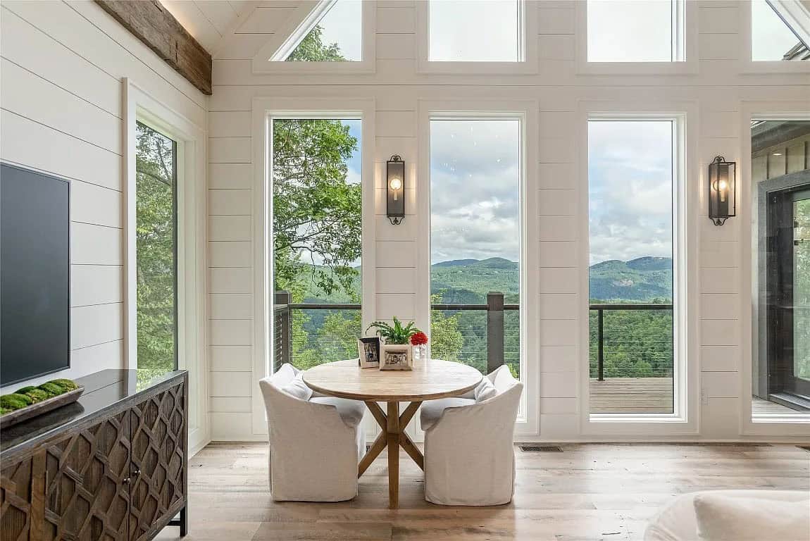 Breakfast nook with round wood table and white chairs beside floor-to-ceiling windows overlooking mountain ridgeline