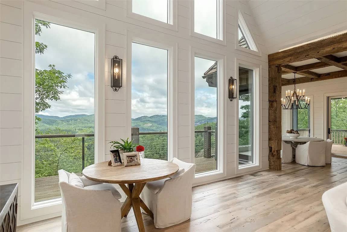 Sunlit sitting area with small round dining table facing tall windows with Blue Ridge Mountain views and reclaimed wood beam accent