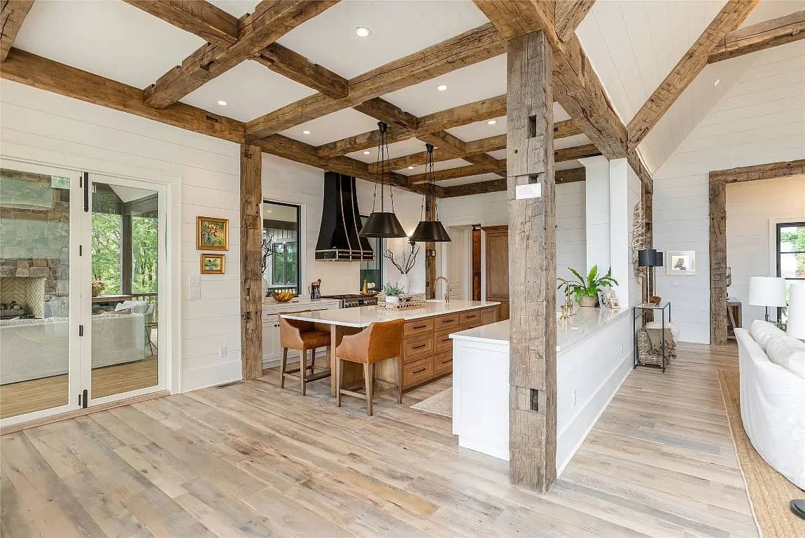 Kitchen and great room with reclaimed wood beam columns, white island, leather barstools, black range hood, and light hardwood floors