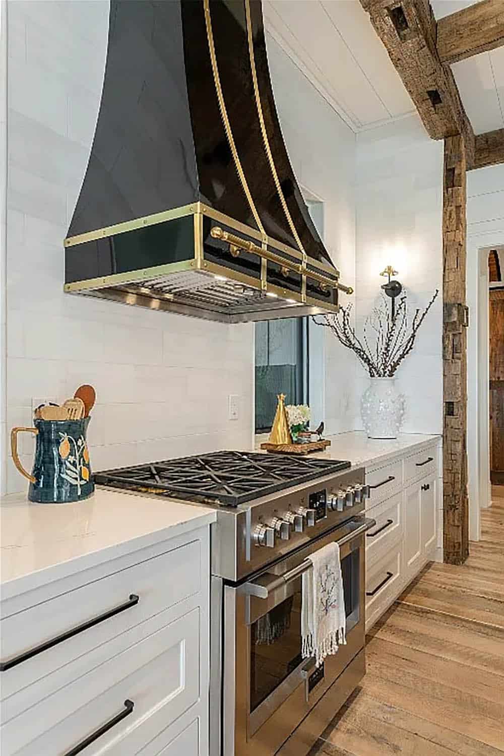 Close-up of black and brass French country range hood above stainless six-burner range with white shiplap backsplash