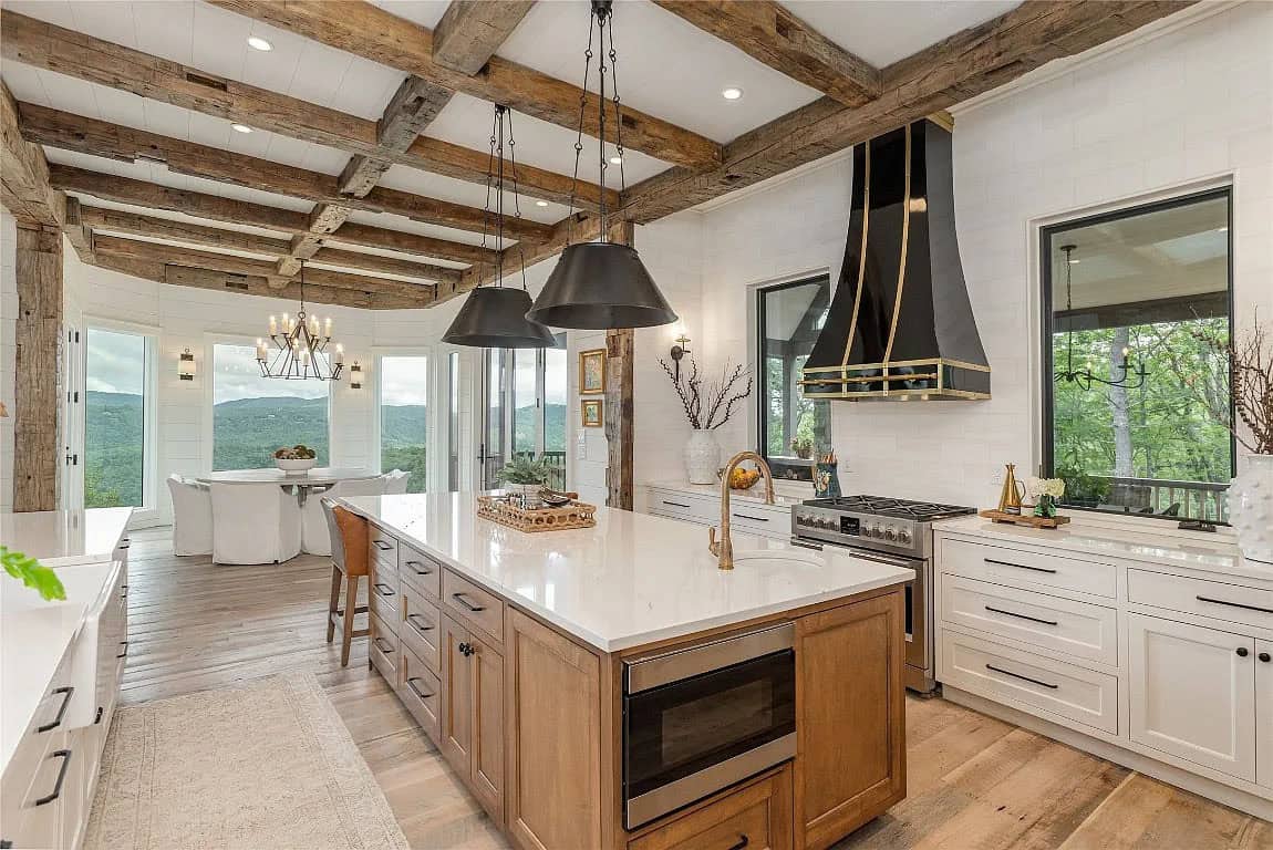 Kitchen with reclaimed beam ceiling, wood island, black and brass range hood, brass faucet, and mountain views through dining area