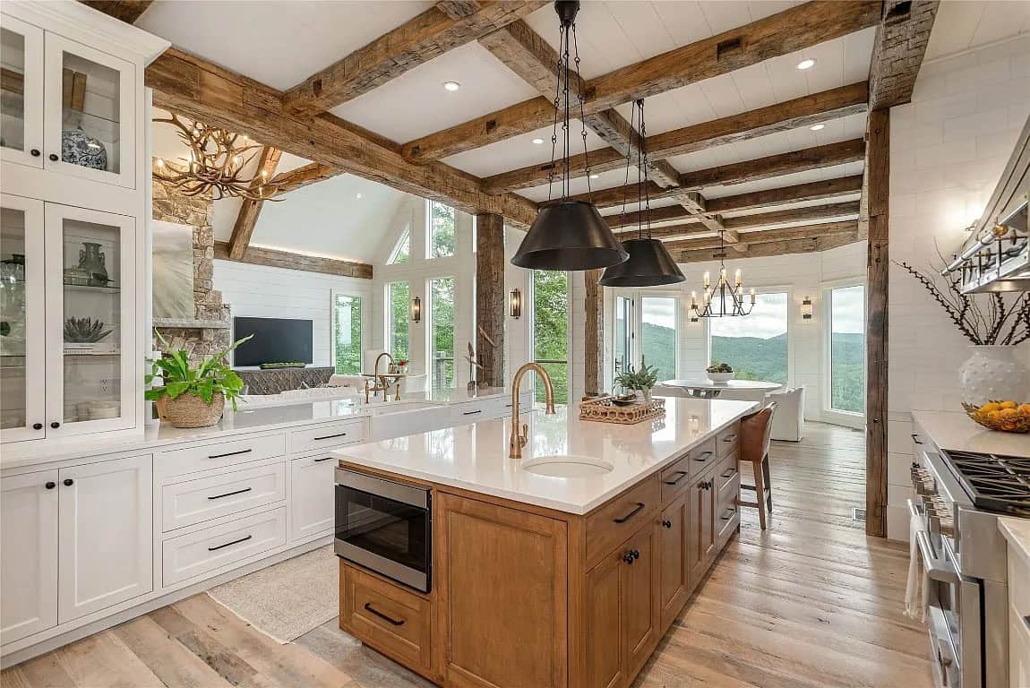 Open kitchen with wood island, dual black pendants, glass-front cabinets, and views through to living room stone fireplace and antler chandelier