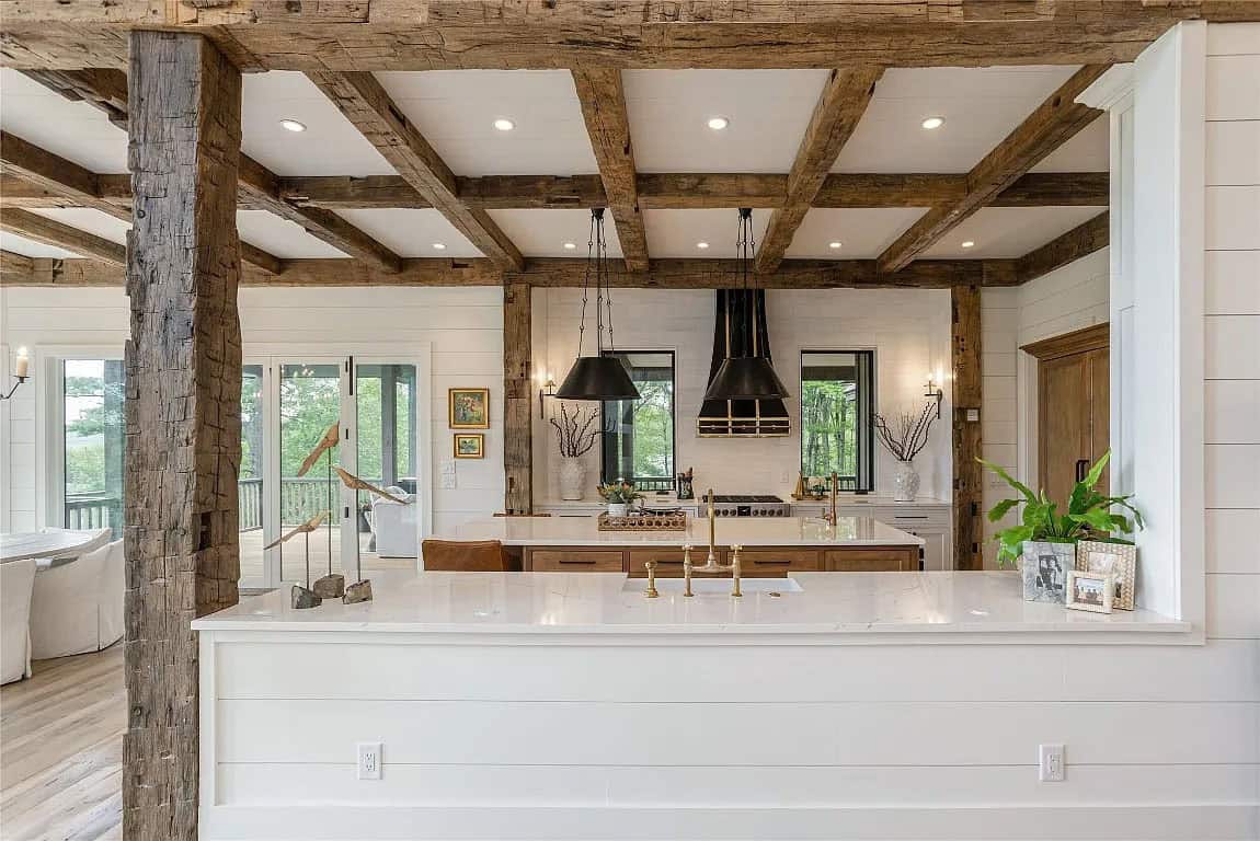 Kitchen viewed through reclaimed timber post framing, showing white quartz peninsula, black range hood, and black iron pendants