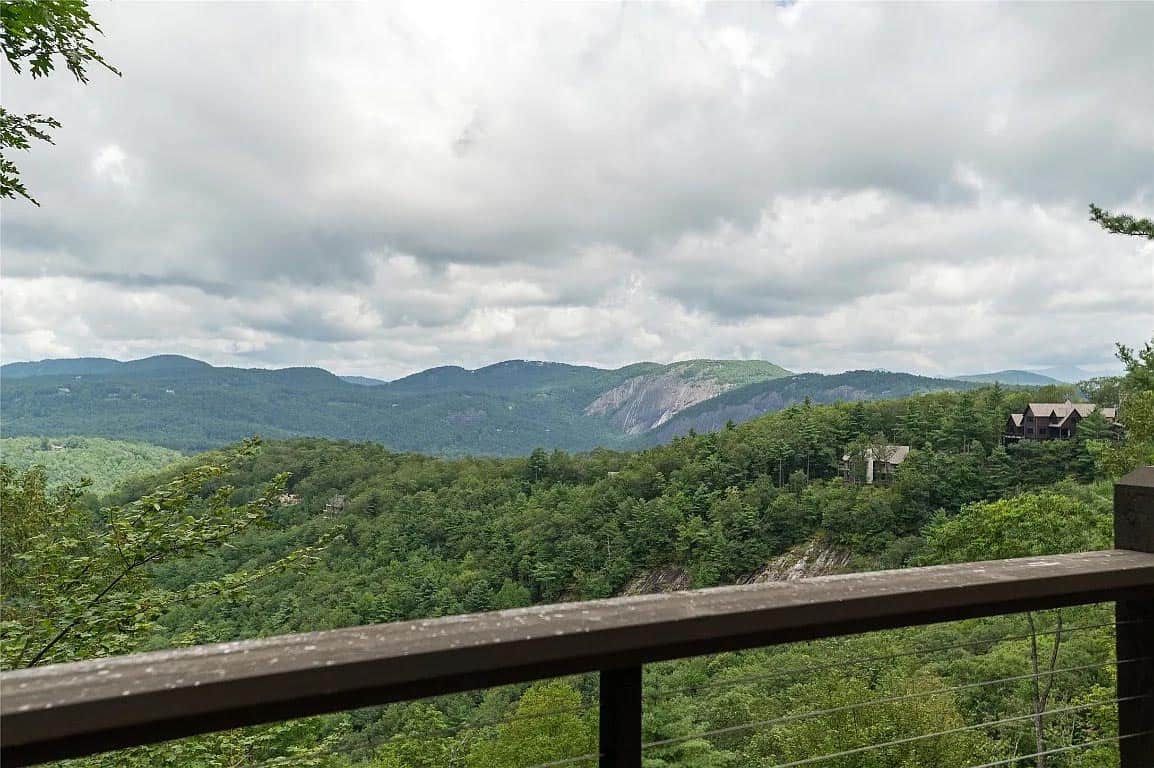 Panoramic view of layered Blue Ridge Mountain ridgelines and dense forest with rocky outcropping from covered deck