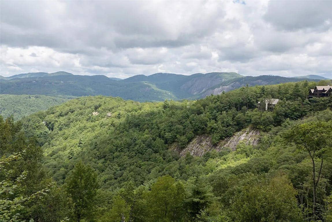 Sweeping aerial-style view of forested North Carolina mountain valley with rock face and distant Blue Ridge peaks
