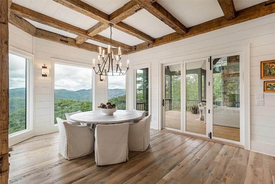 Dining area with reclaimed beam coffered ceiling, round table, slipcovered chairs, iron chandelier, and French doors opening to covered porch