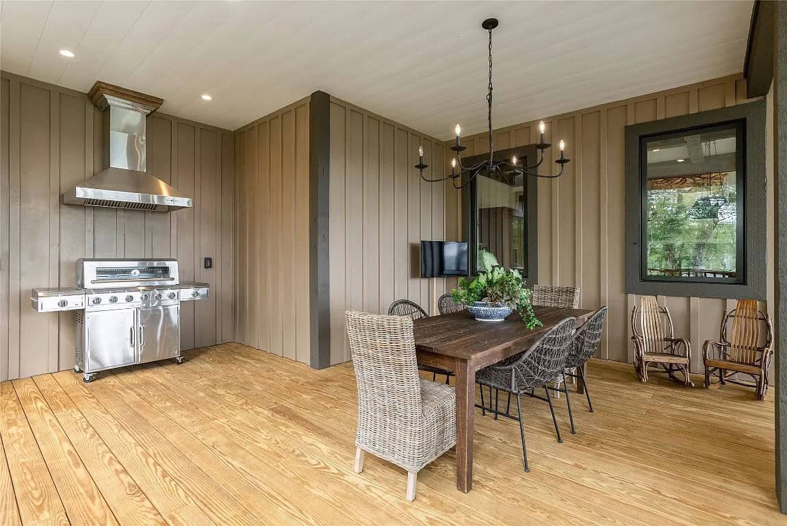 Covered outdoor kitchen and dining area with stainless grill, range hood, wood farm table, wicker chairs, and wood plank ceiling