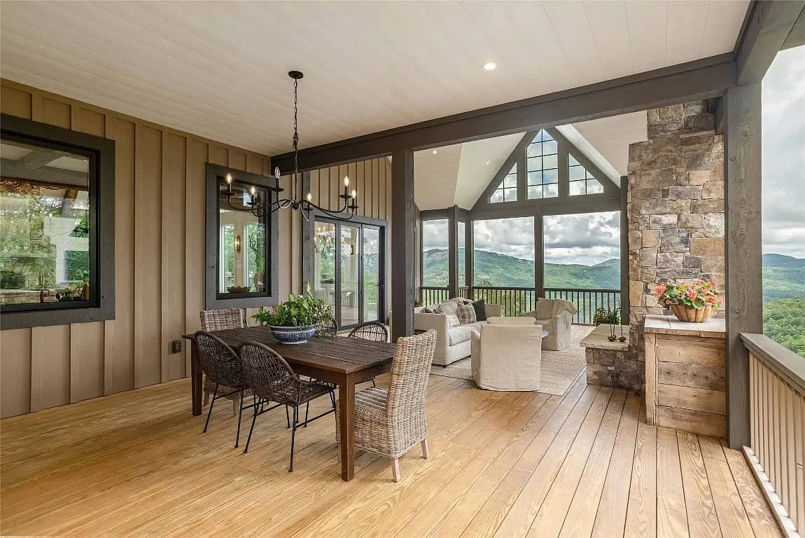Covered porch with dining and lounge areas, stone fireplace column, board-and-batten siding, and mountain views through open gable end
