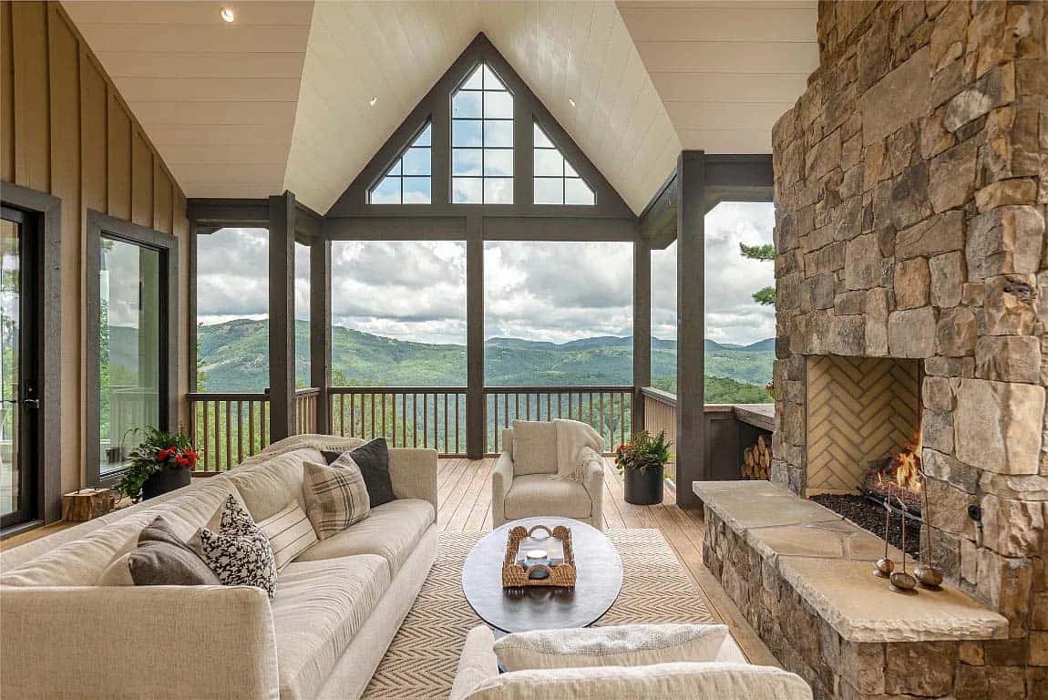 Screened porch living area with cream sofas, stone fireplace with herringbone firebox, vaulted shiplap ceiling, and panoramic mountain views