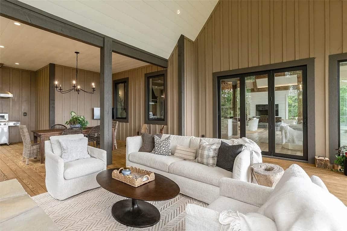 Covered lower porch lounge with cream sofas, board-and-batten walls, iron chandelier, and sliding glass doors to upper level
