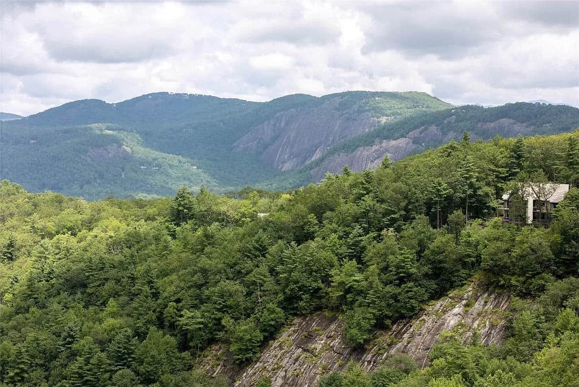 View of large granite rock face and densely forested North Carolina mountain valley with distant Blue Ridge peaks