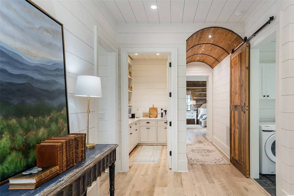 Hallway with reclaimed wood arched barn door, mountain landscape painting, antique console table, and view into pantry and bedroom