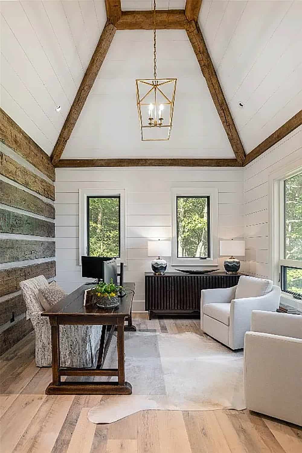 Home office with vaulted shiplap ceiling, reclaimed beam accents, log wall, gold lantern pendant, wood desk, and cowhide rug