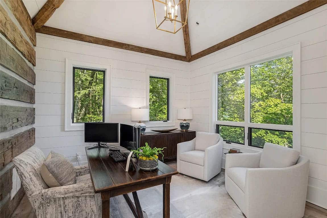 Home office with log accent wall, vaulted shiplap ceiling, reclaimed wood beams, gold lantern pendant, wood desk, and forest views