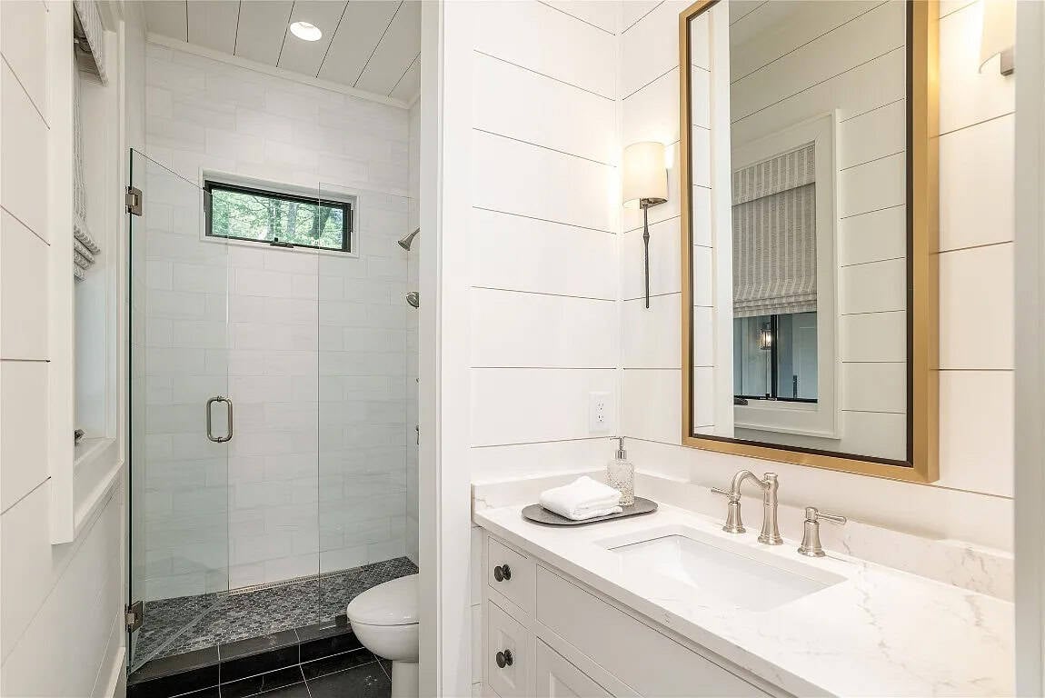 Guest bathroom with white subway tile walk-in shower, gold-framed vanity mirror, white quartz countertop, and shiplap walls