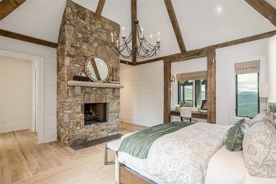 Primary bedroom with floor-to-ceiling stone fireplace, vaulted shiplap ceiling, reclaimed beams, iron chandelier, and mountain view sitting nook