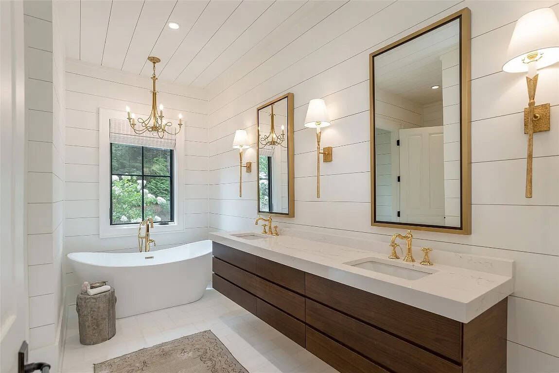 Primary bathroom with floating dark wood double vanity, gold fixtures, dual gold-framed mirrors, brass sconces, and freestanding soaking tub