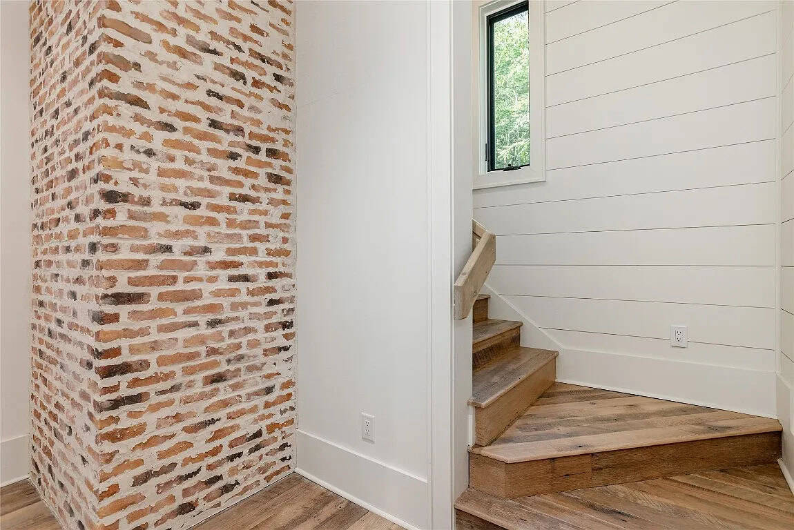Stairwell with exposed antique brick accent wall, reclaimed wood stair treads, white shiplap walls, and black-framed clerestory window