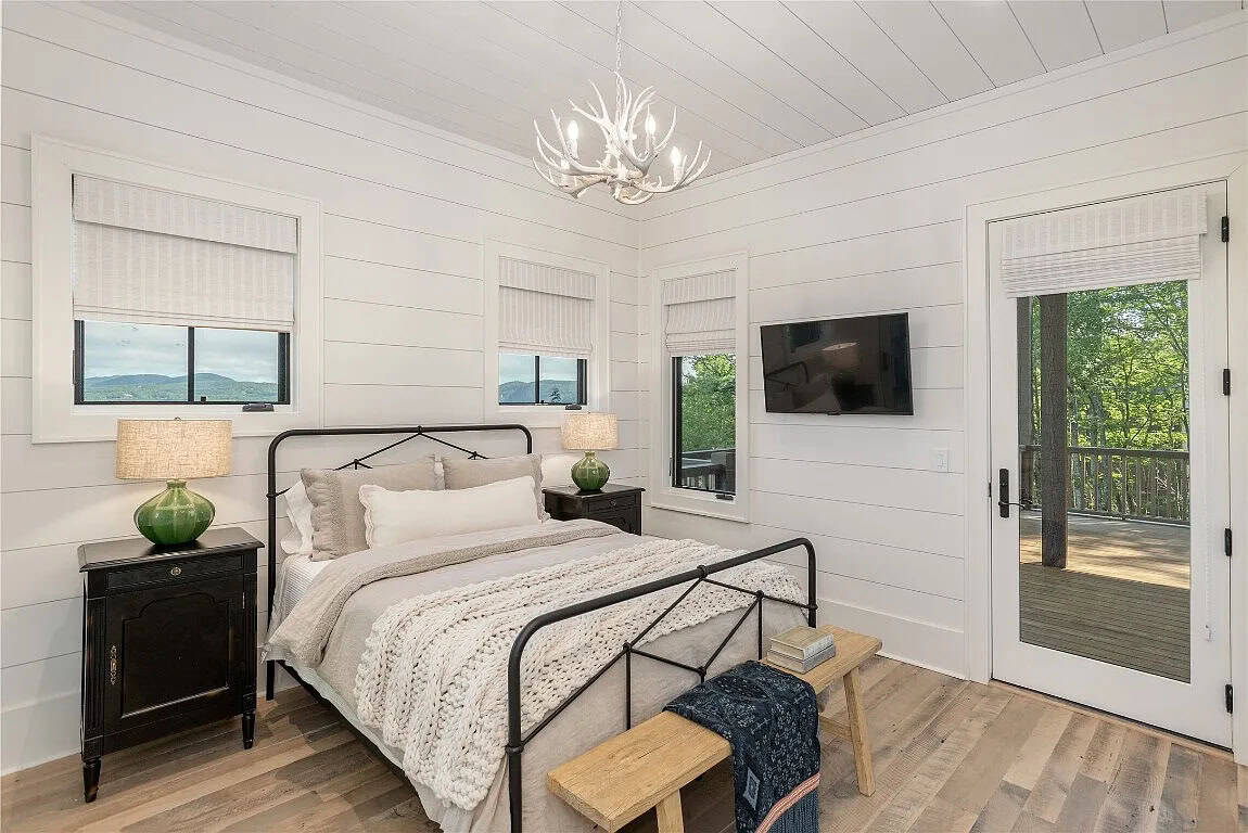 Guest bedroom with black iron bed, chunky knit throw, white antler chandelier, green ceramic lamps, shiplap walls, and deck access door