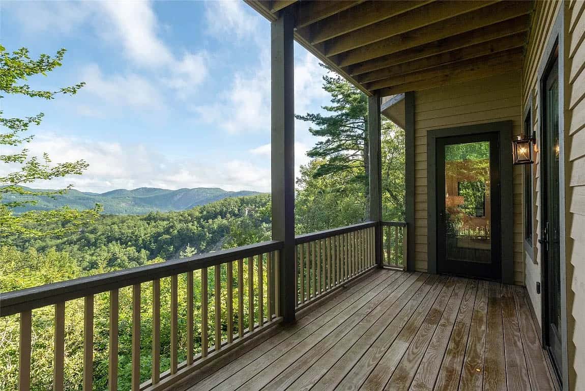 Lower level bedroom deck with wood plank flooring, dark railing, lantern sconce, and sweeping Blue Ridge Mountain forest views