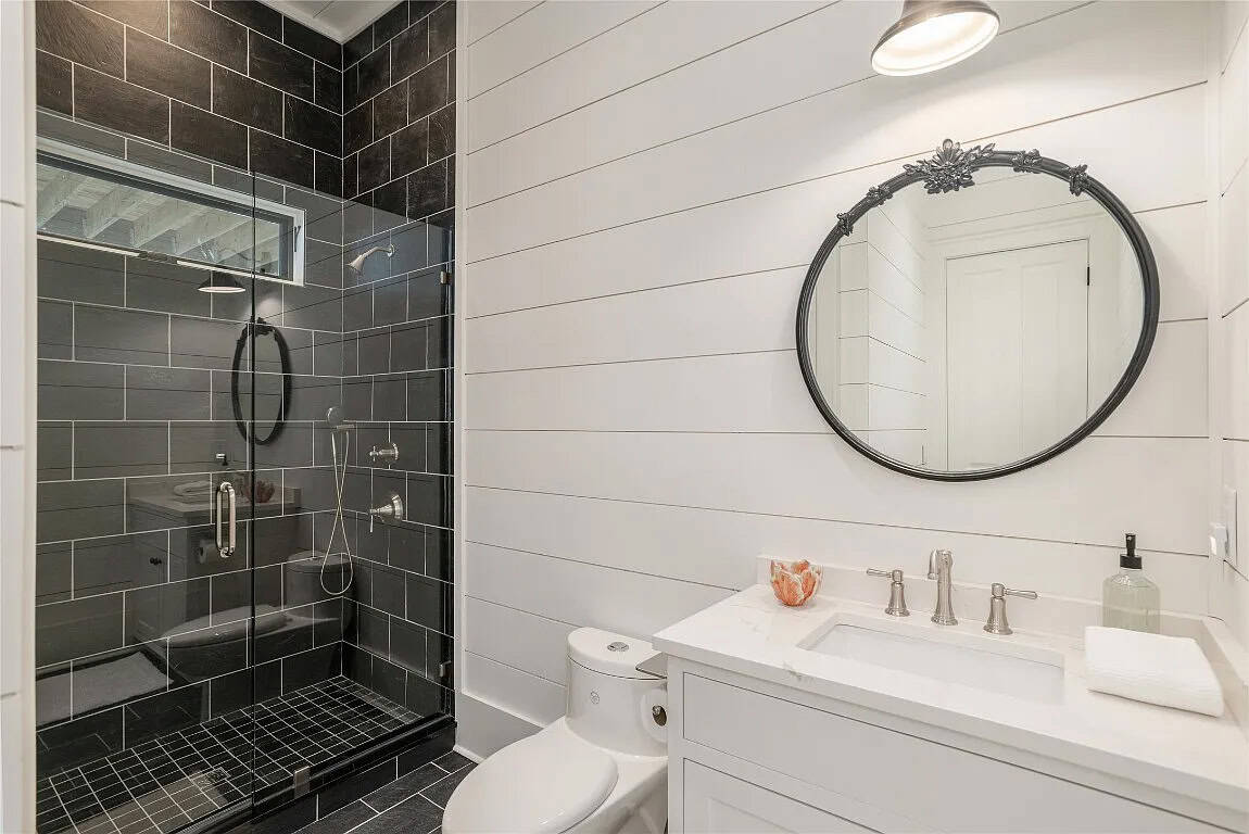 Guest bathroom with floor-to-ceiling black subway tile shower, round ornate black mirror, white vanity, and shiplap walls