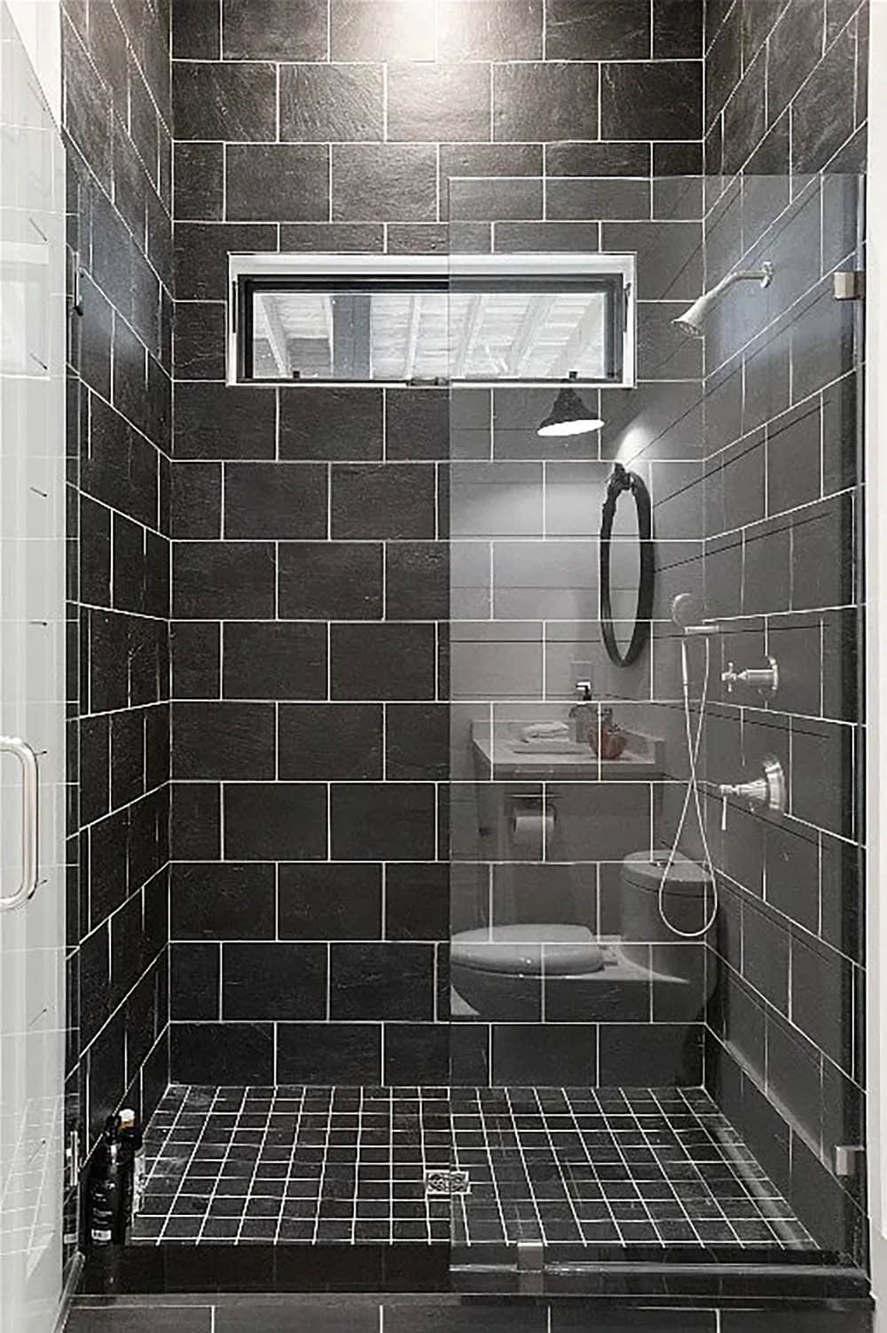 Interior view of black slate tile walk-in shower with mosaic floor, clerestory window, and chrome fixtures