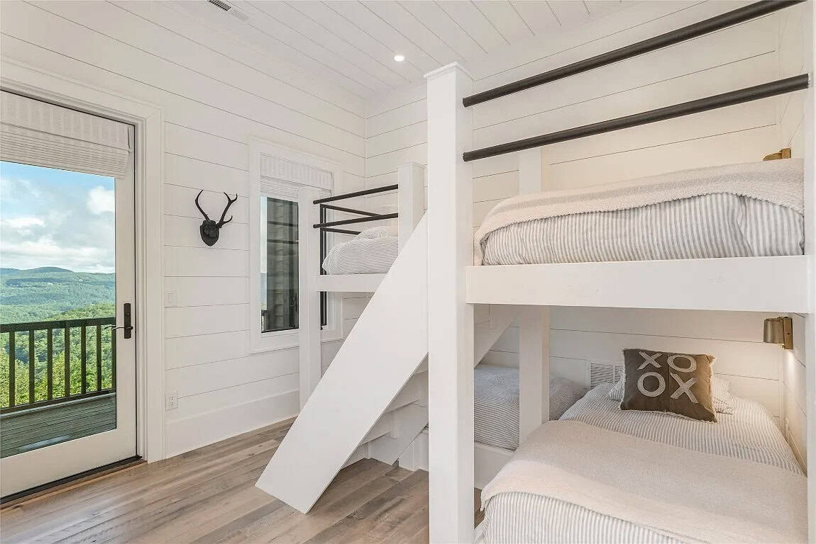 Bunk room with built-in white double bunk beds, black iron rails, stair steps, antler wall mount, and mountain view deck door