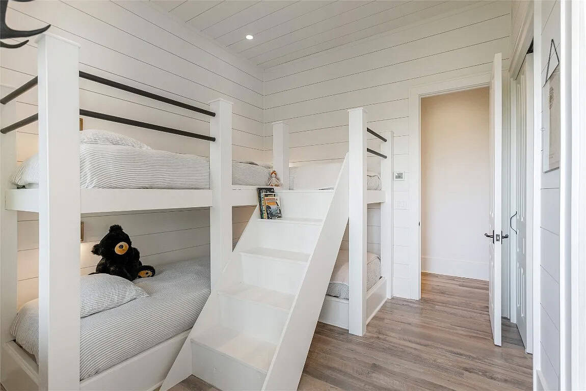 Bunk room with four built-in white bunk beds, center stair, shiplap walls, and hardwood floors