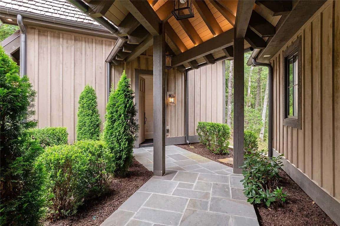 Front entry with bluestone pathway, board-and-batten siding, columned covered porch, lantern sconces, and evergreen landscaping