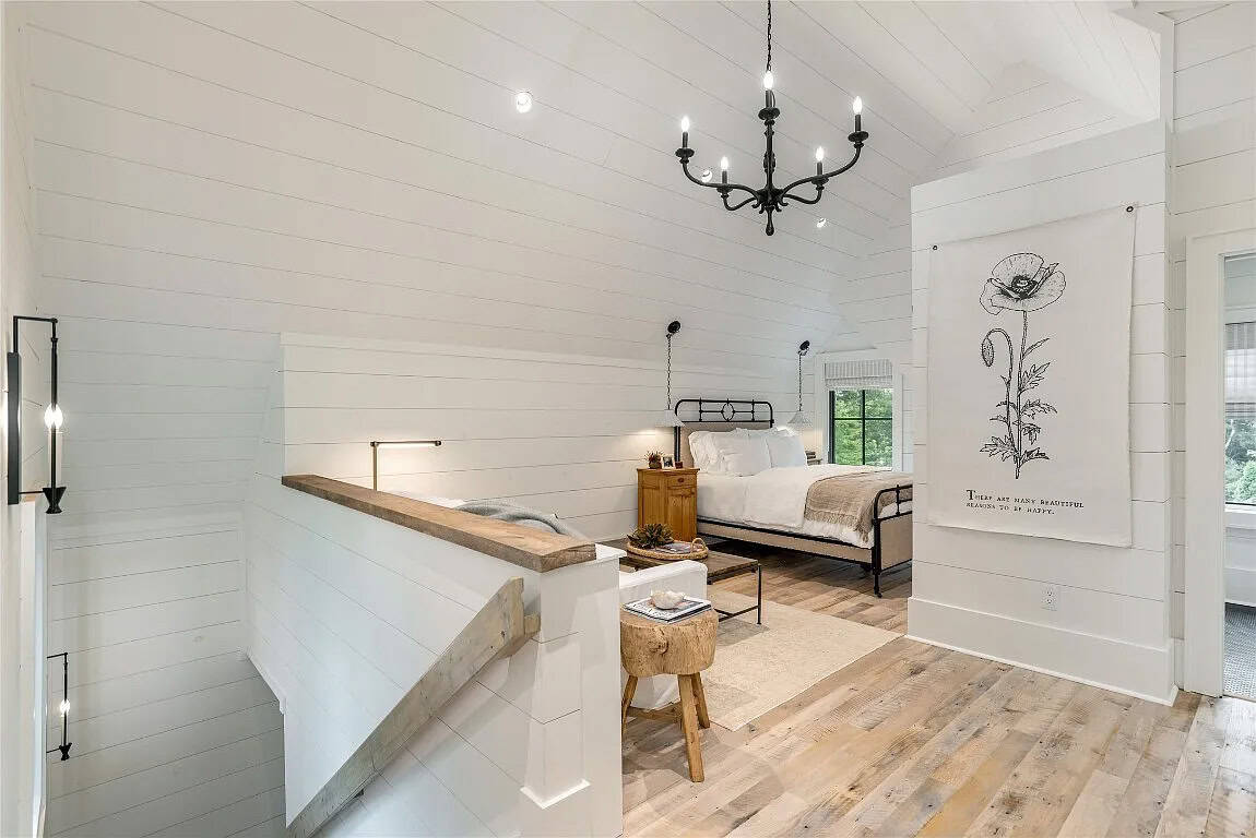 Upper bonus suite stairwell landing opening to bedroom with iron bed, white shiplap walls, vaulted ceiling, and iron chandelier