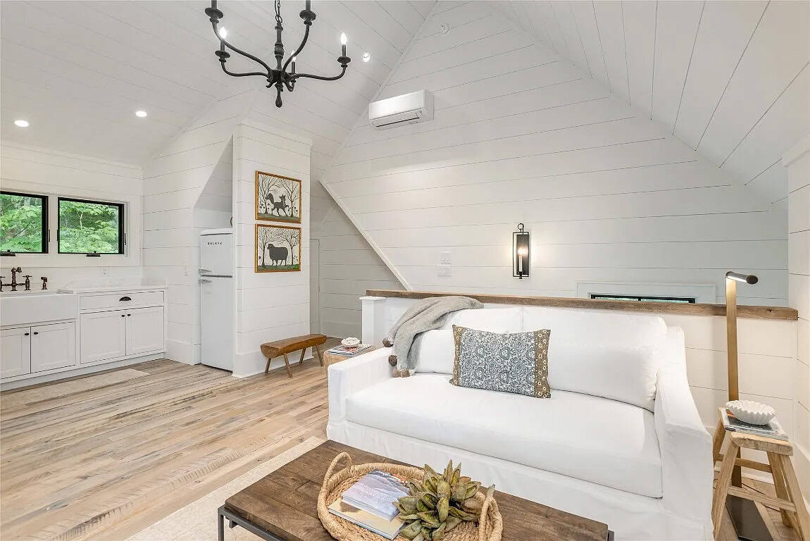 Bonus suite living area with white slipcovered sofa, vaulted shiplap ceiling, iron chandelier, kitchenette, and folk art prints