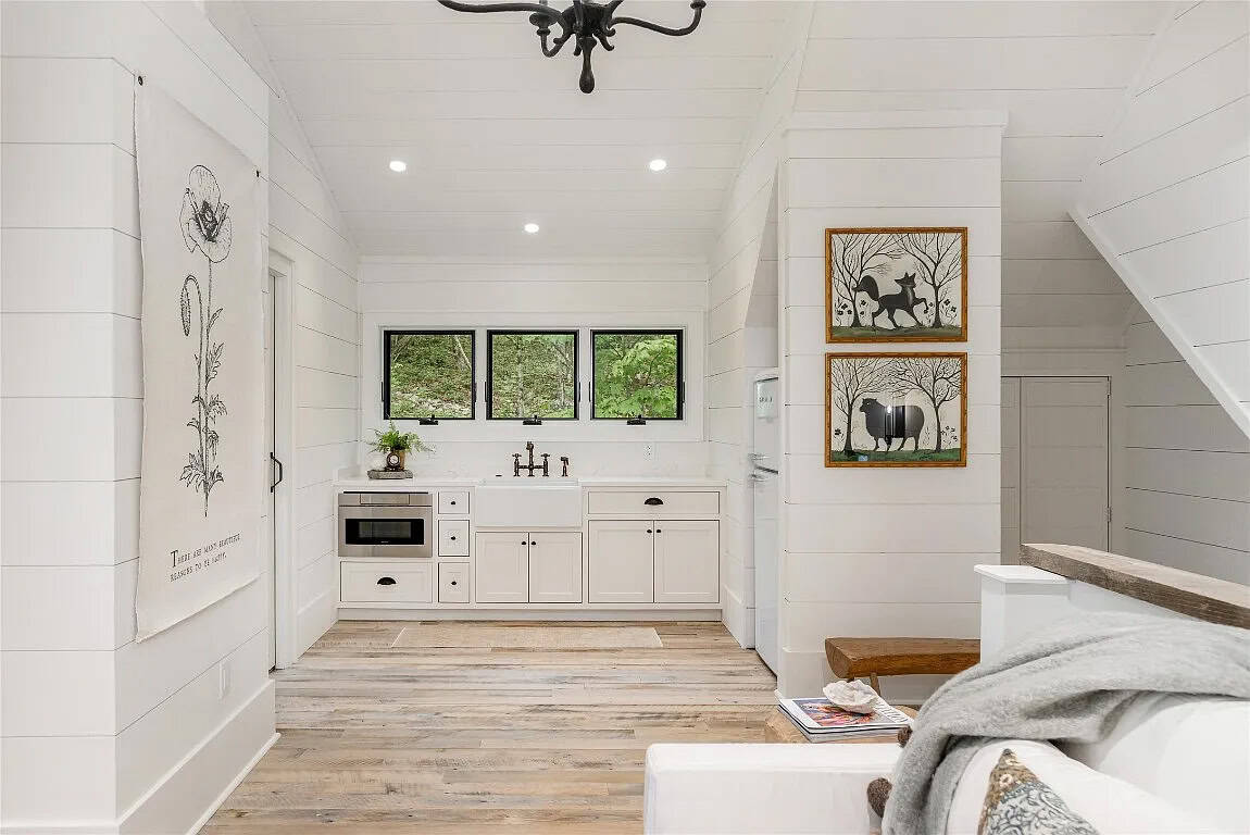Bonus suite kitchenette with white farmhouse sink, bronze bridge faucet, white cabinetry, microwave, and triple black-framed windows