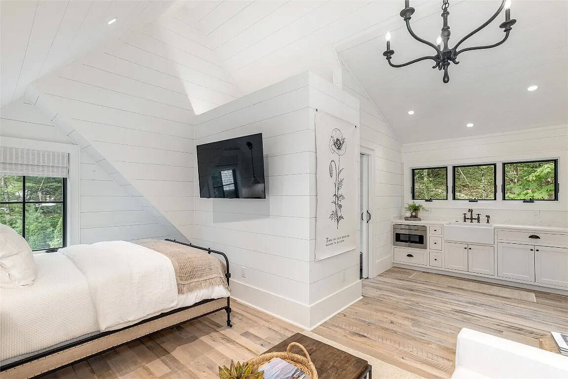 Bonus suite bedroom with iron bed, vaulted shiplap ceiling, wall-mounted TV, iron chandelier, and adjacent kitchenette