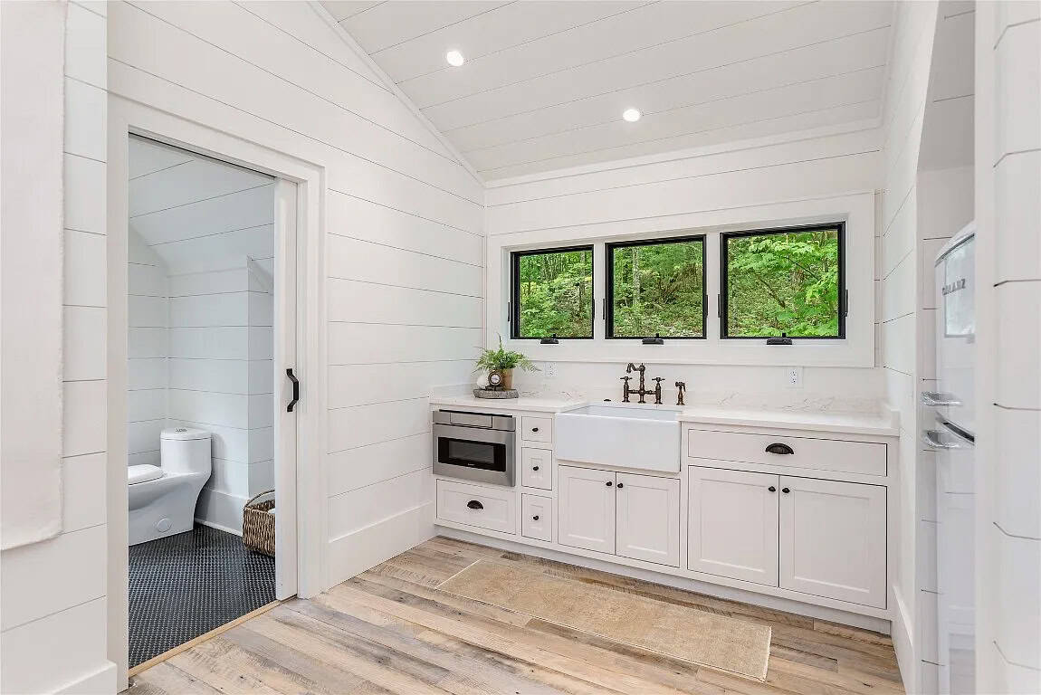 Bonus suite kitchenette close-up with farmhouse sink, bronze faucet, microwave drawer, white shaker cabinets, and bathroom beyond
